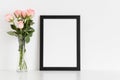 Black frame mockup with a bouquet of pink roses in a glass vase on a white table. Portrait orientation Royalty Free Stock Photo