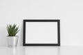 Black frame mockup with a cactus in a pot on a white table.Landscape orientation Royalty Free Stock Photo