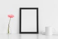 Black frame mockup with a chrysanthemum in a vase, book and a mug on a white table. Portrait orientation Royalty Free Stock Photo