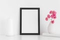 Black frame mockup with pink roses in a vase and candle on a white table.Portrait orientation Royalty Free Stock Photo