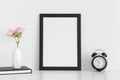 Black frame mockup with workspace accessories  and pink roses in a vase on a white table.Portrait orientation Royalty Free Stock Photo