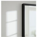 A black-framed rectangular mirror is mounted on a plain light-colored wall. Soft Royalty Free Stock Photo