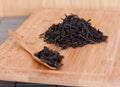 Black friable tea in a wooden spoon and on a wooden tray