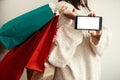 Black Friday. Christmas Sales. Happy Girl holding phone with empty screen and carrying colorful shopping bags on white background Royalty Free Stock Photo