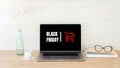 Black Friday concept. Laptop screen with text sign `Black Friday` and shopping cart on women workplace