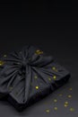 Black friday gift box wrapped in fabric with golden confetti. Traditional Japanese gift wrapping furoshiki style. Eco friendly
