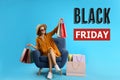 Black Friday Sale. Beautiful young woman with shopping bags sitting in armchair on light blue background Royalty Free Stock Photo