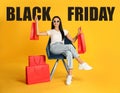 Black Friday Sale. Beautiful young woman with shopping bags sitting in armchair on yellow background Royalty Free Stock Photo