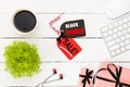 Black Friday Sale text on a red and black tag with coffee cup, plant table, gift box Earphone and mouse keyboard on white wooden Royalty Free Stock Photo