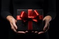 Black Friday sale. Young woman hands holding black gift box with red satin bow on black background. Black Friday sale, promotion, Royalty Free Stock Photo