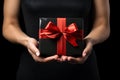 Black Friday sale. Young woman hands holding black gift box with red satin bow on black background. Black Friday sale, promotion, Royalty Free Stock Photo
