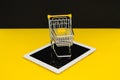 Black Friday sales. Small shopping trolley on a tablet in yellow background. Cybermonday concept