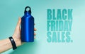 Black Friday sales text near female hand holding aluminum thermo water bottle of blue. Background of cyan, Aqua menthe color. Royalty Free Stock Photo