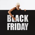 Black Friday shopping. Smiling black woman pointing at a Black Friday text on advertising banner commercial sign. Store and mall Royalty Free Stock Photo