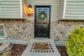 Black front door with wreath of house with stone wall and gray exterior siding