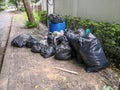 Black garbage bag pile near municipal trash bin full on sidewalk Royalty Free Stock Photo