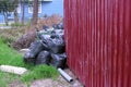 Black garbage bags near the fence of private house and an overturned trash can. Royalty Free Stock Photo