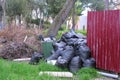 Black garbage bags near the fence of private house and an overturned trash can. Royalty Free Stock Photo