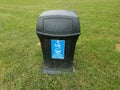 Black garbage can on green grass with blue soda plastic beverage container sign