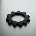 A black gear-shaped object rests on a textured, metallic surface. The gear has a Royalty Free Stock Photo
