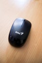Black genius wireless mouse on wooden background, top view, close up. Genius designs and creates PC gaming and mobile products