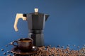 Black geyser coffee maker, coffee beans and a cup with coffee on a blue background. Royalty Free Stock Photo