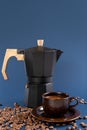 Black geyser coffee maker, coffee beans and a cup with coffee on a blue background. Royalty Free Stock Photo