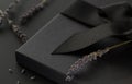 Black gift box on a dark contrasted background, decorated with a textured bow and lavender