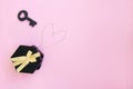 Black gift box with gold bow with chain lined in the shape of a heart and a black key on pink background Royalty Free Stock Photo