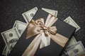 Black gift box with gold ribbon and a big bow on a pile of money. Gift on a granite surface Royalty Free Stock Photo