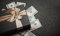 Black gift box with gold ribbon and a big bow on a pile of money. Gift on a granite surface Royalty Free Stock Photo