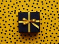 A Black Gift Box With A Golden Ribbon On Yellow Polka Dot Background.