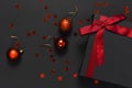 Black gift box with red ribbon, Christmas balls, red holographic glitter confetti on dark background top view flat lay. Holiday Royalty Free Stock Photo