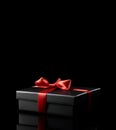 Black gift box with red satin ribbon bow isolated on black Royalty Free Stock Photo