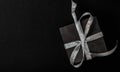 Black gift box with silver ribbon bow on black background. Top view, copy space Royalty Free Stock Photo