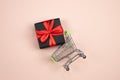 Black gift box tied with red ribbon in a shopping cart. Cart with purchases. Present concept. Royalty Free Stock Photo