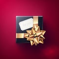 The black gift box with the white greeting card and glittering golden bow with ribbons isolated on red background Royalty Free Stock Photo