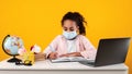 Black girl in mask sitting at desk writing in nootebook