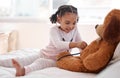 A black girl playing hospital doctor with a teddy bear on her bed, holding a stethoscope and imagining a kid. Child Royalty Free Stock Photo