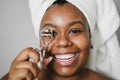 Black girl using eyelash curler while wearing body towel - Main focus on eyes