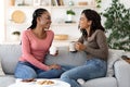Black girlfriends enjoying weekend together, drinking coffee on couch