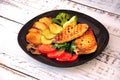 A black glass plate with two grilled chicken fillet steaks with potatoes, broccoli, zucchini, tomato and mushrooms on a wooden Royalty Free Stock Photo