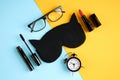 Black glasses, alarm clock, mascara, pomade and sleep mask on blue and yellow background composition Royalty Free Stock Photo