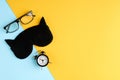 Black glasses, alarm clock and sleep mask on blue and yellow background composition Royalty Free Stock Photo