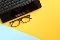 Black glasses and laptop keyboard on blue and yellow background composition Royalty Free Stock Photo