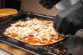 A black-gloved chef prepares pizza