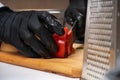 A black-gloved chef slices a tomato into thin slices on a wooden Board with a knife