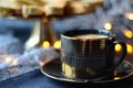 Black gold coffee cup with a platter of cookies and lights in the background