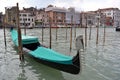 Black gondola covered in green anchored at poles in the Grand Canal of Venice.