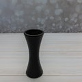 A black graceful ceramic flower vase stands on a wooden table